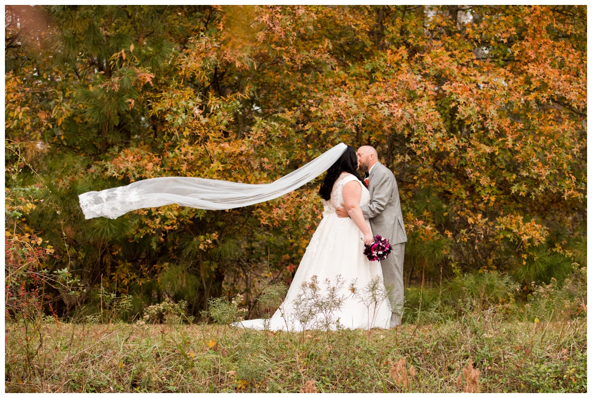 Fall portrait of bride and groom surrounded by trees and veil blowing in the wind. Veil shot.