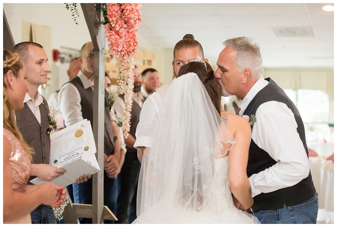 Indoor wedding ceremony. Bride's father giving her away to the groom. Father kissing the bride. Maryland wedding at Circle D Farm in Woodbine. Maryland Wedding Photographer