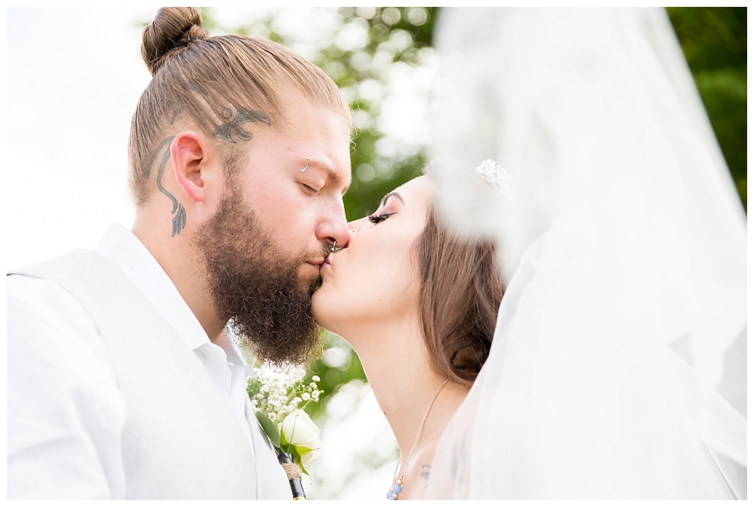 Outdoor bride and groom portraits. Bride and groom kissing under veil next to a field. Maryland wedding at Circle D Farm in Woodbine. Maryland Wedding Photographer.